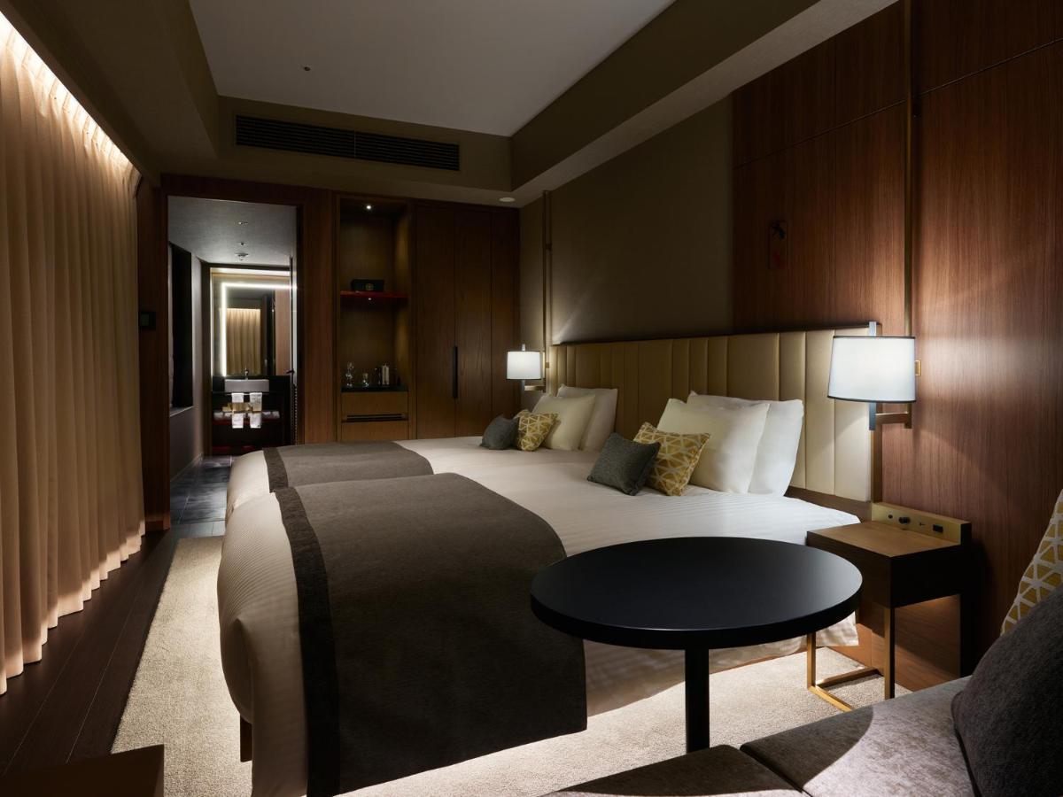 Mitsui Garden Hotel Roppongi Tokyo Premier Экстерьер фото The photo shows a stylish hotel room featuring two beds with plush bedding and decorative pillows. The walls are made of wood, creating a warm and modern atmosphere. There are bedside lamps on each side of the beds providing soft lighting. A small ro