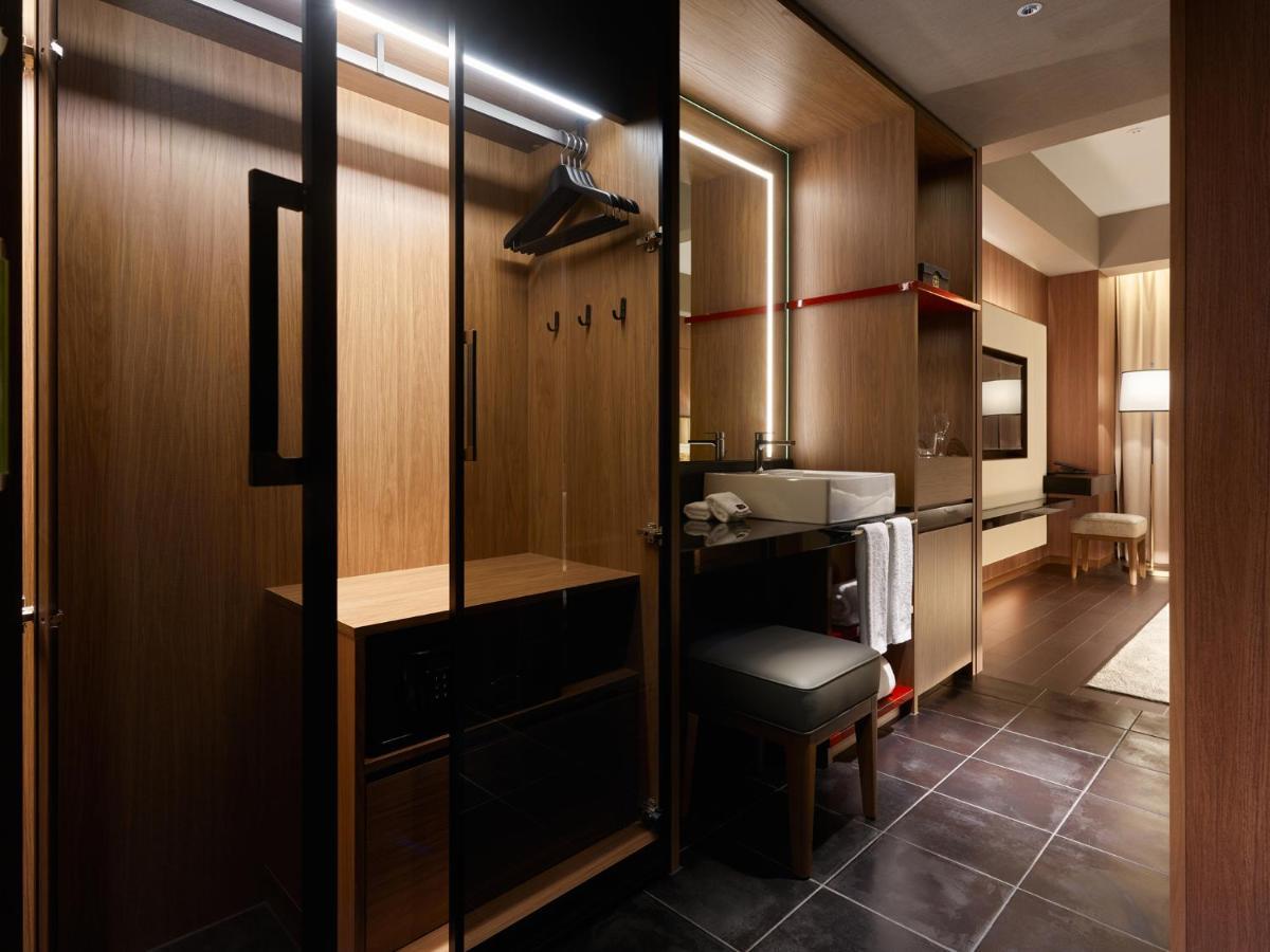 Mitsui Garden Hotel Roppongi Tokyo Premier Экстерьер фото The photo depicts a modern and stylish hotel room's closet area. It features wooden cabinetry with a sleek finish, including mirrored doors. Inside, there are hangers for clothing and hooks mounted on the wall. A small bench or chair is positioned ne