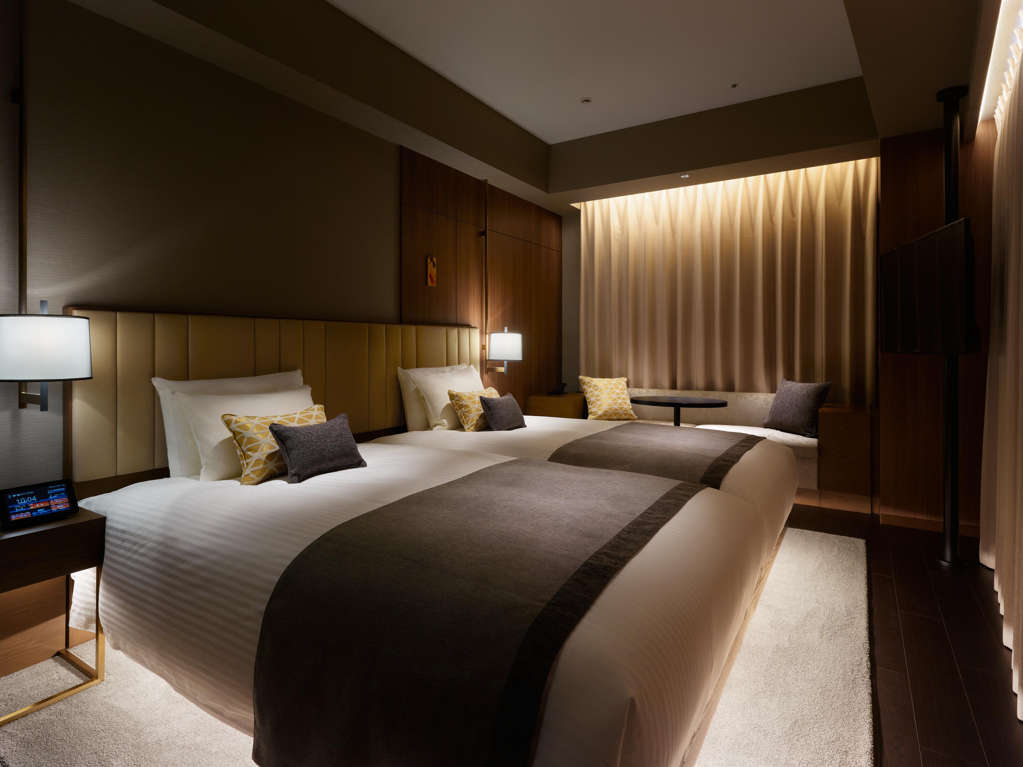 Mitsui Garden Hotel Roppongi Tokyo Premier Экстерьер фото The photo shows a modern hotel room featuring two beds with plush white linens and decorative pillows. The room has a warm and inviting ambiance, highlighted by soft lighting from lamps and the backlit curtains. There is also a small table with chair