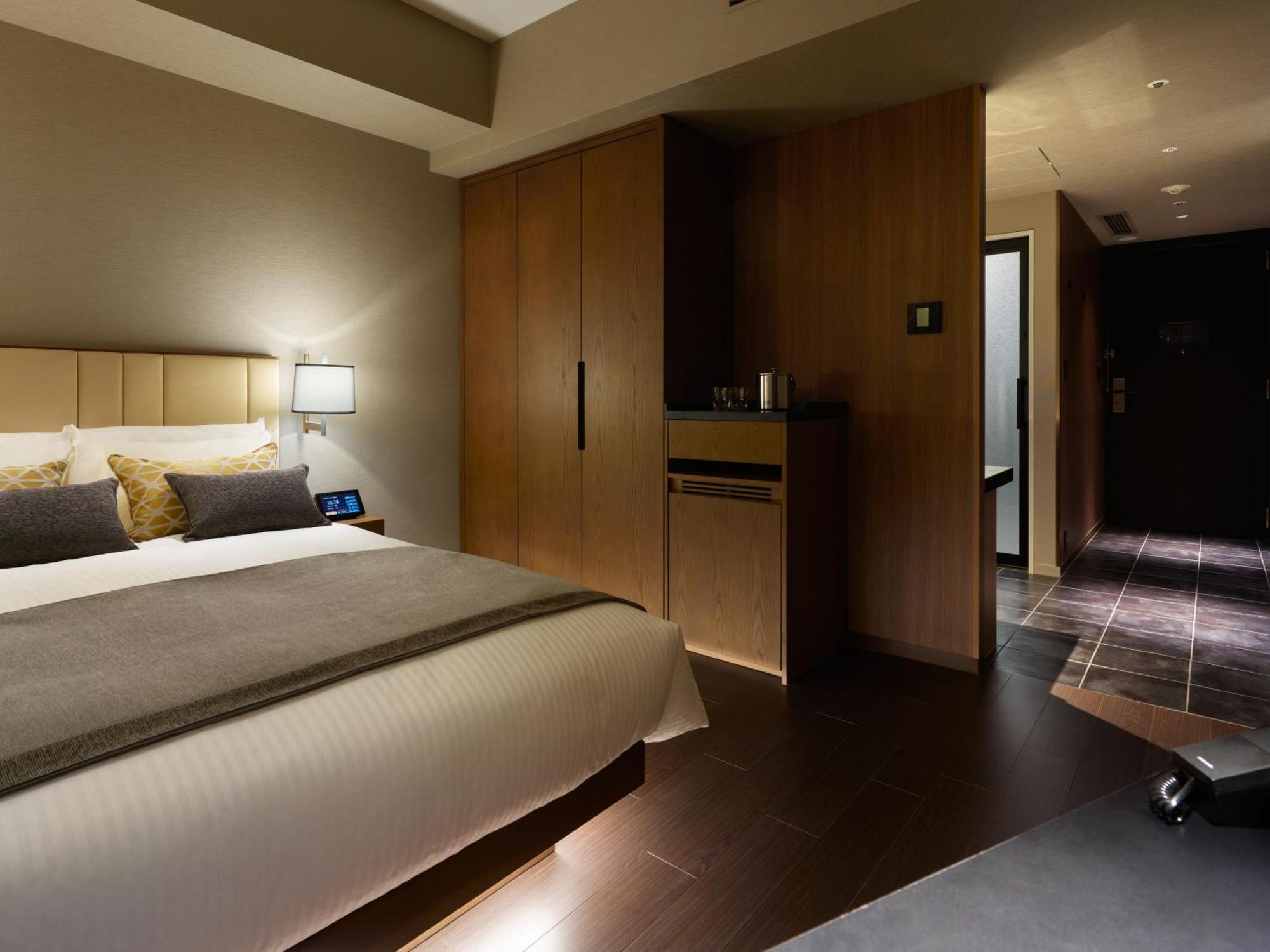 Mitsui Garden Hotel Roppongi Tokyo Premier Экстерьер фото The photo shows a modern hotel room featuring a neatly made bed with decorative pillows. The room has wooden accents, including a wardrobe and cabinetry, contributing to a warm ambiance. A bedside lamp is on one side of the bed, and there's a small a
