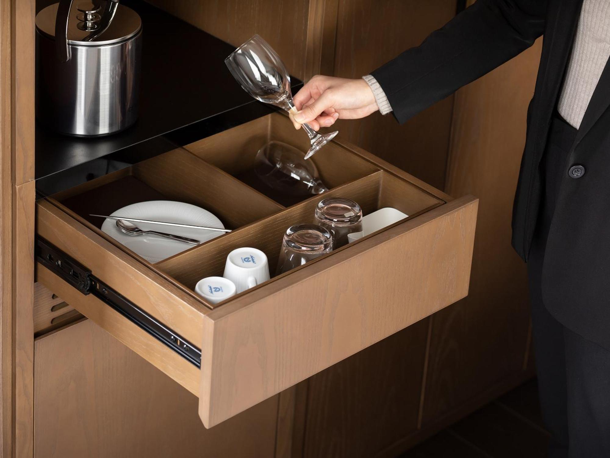 Mitsui Garden Hotel Roppongi Tokyo Premier Экстерьер фото The photo depicts a wooden kitchen drawer being pulled open, revealing a neatly organized selection of dishware. Inside, there are glass cups, a wine glass being held by a person, and plates. The setting appears modern and sleek, with a sophisticated